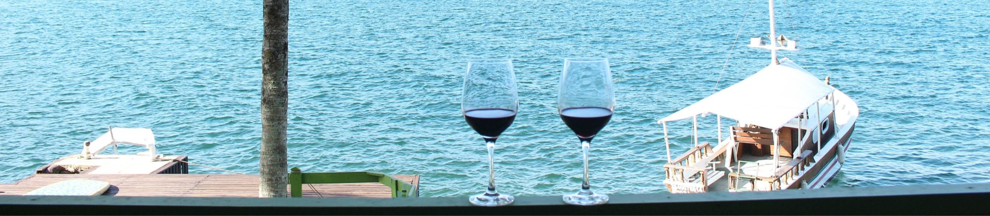 Duas taças de vinho na varanda, de frente para o mar e o barco da casa